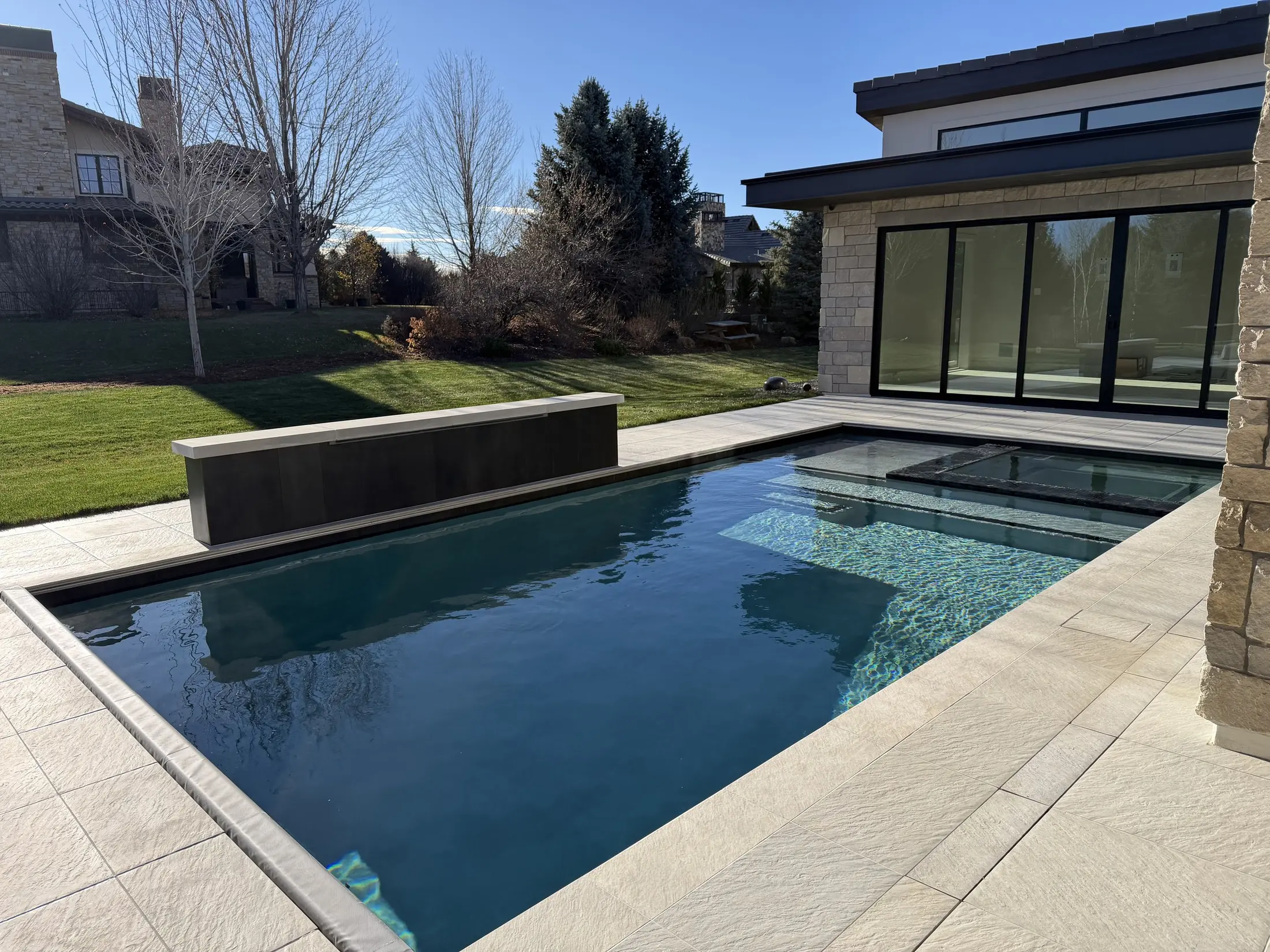 Dark-bottom pool with a raised spa and spillway beside a contemporary stone residence