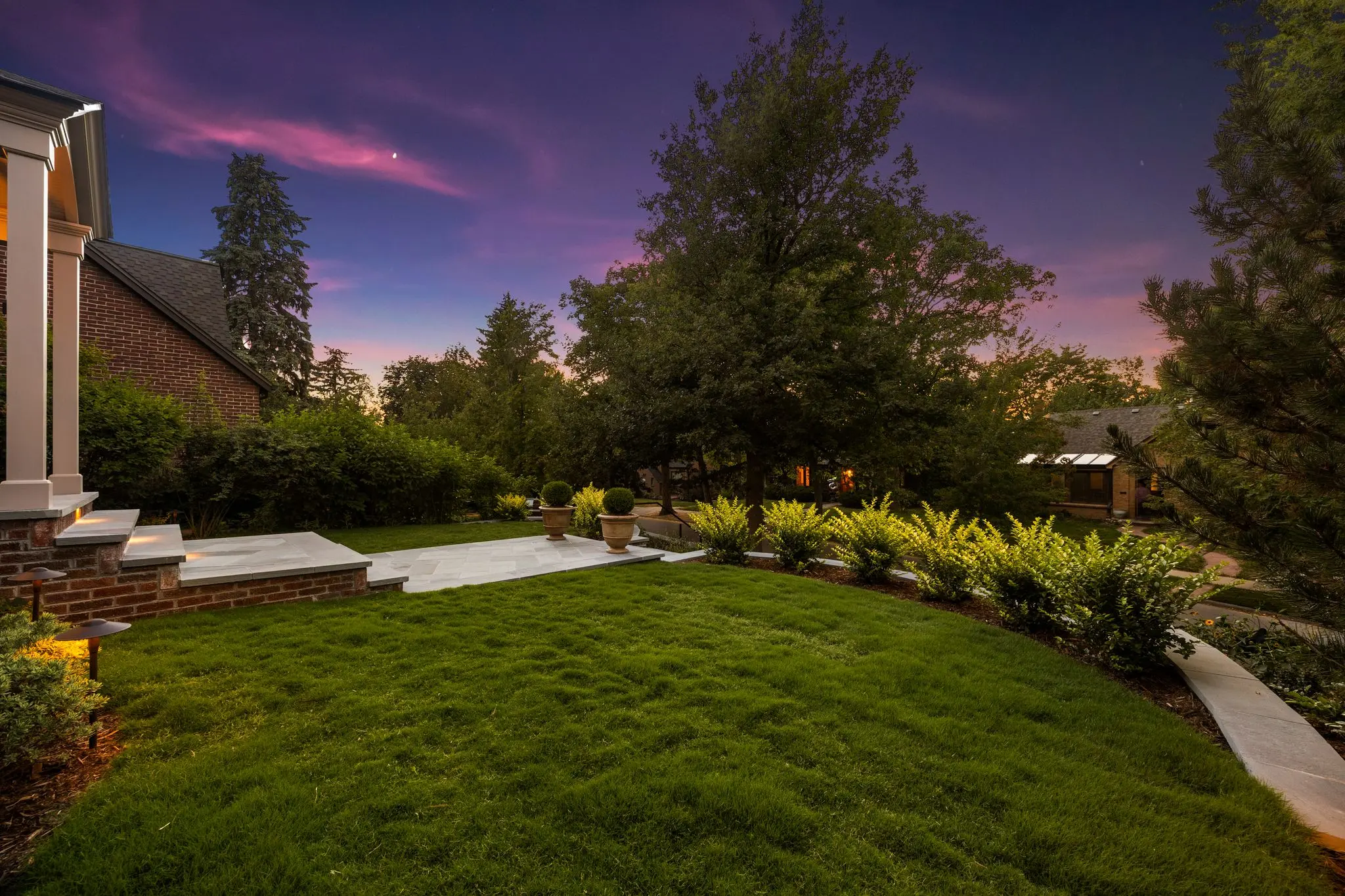 Lit lawn and planting beds beneath a twilight sky