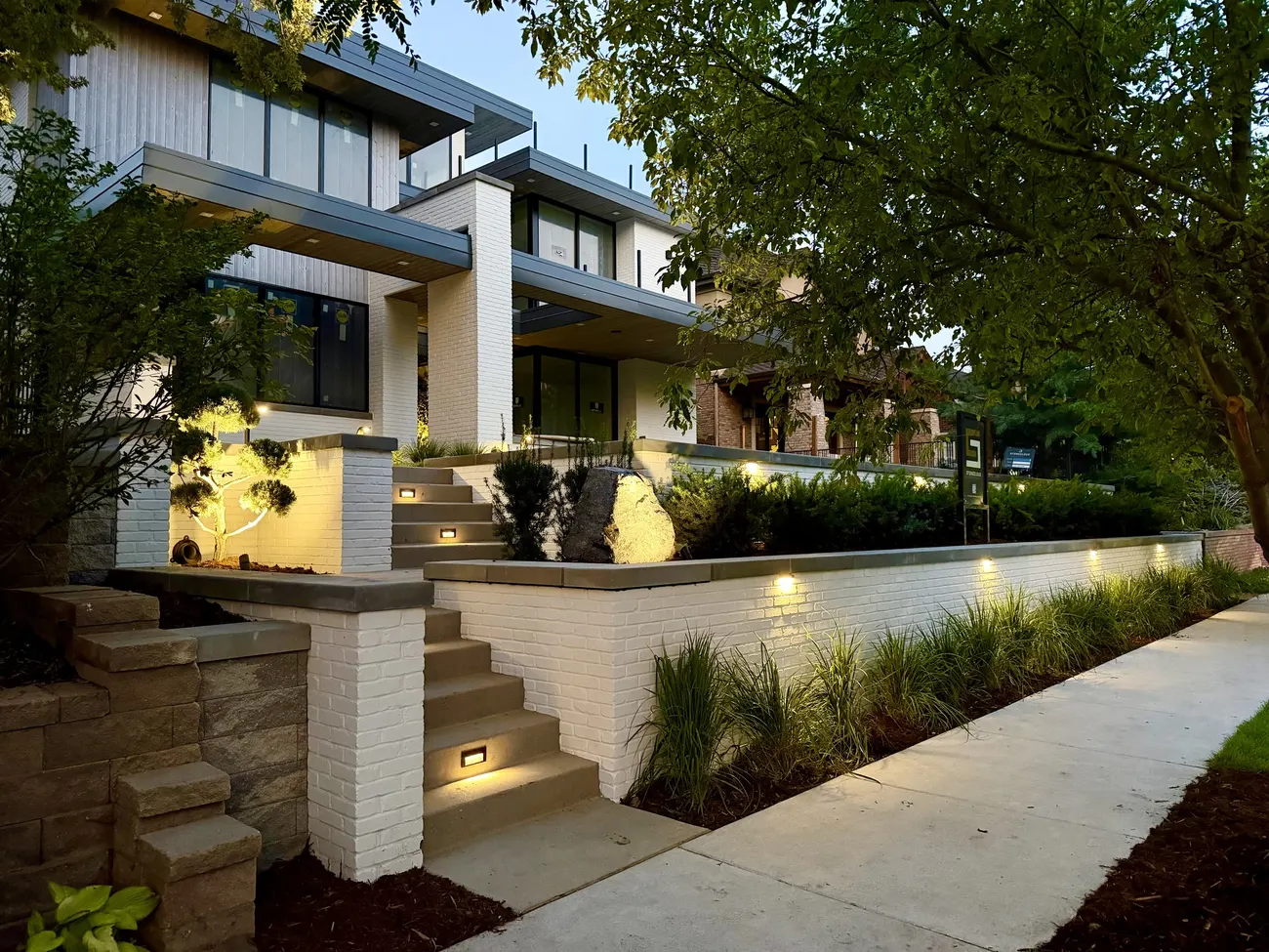Lit entry walk and planting against a contemporary house at dusk