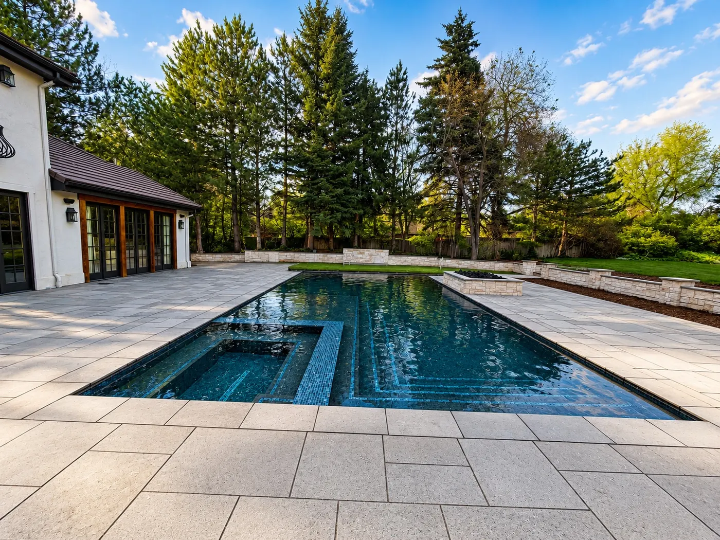 Glass-tiled pool with an in-water bench, large-format stone decking and a stone fire bowl